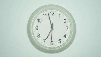 White wall clock says 2 minutes until 7 o'clock in the morning. The time passed slowly in a day. on white background. video