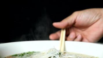 Noodles in a bowl are hot with chopsticks. The heat emanated from the noodles. On the black background. video