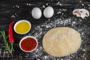 Raw dough for pizza with ingredients and spices on black background photo