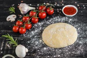 Raw dough for pizza with ingredients and spices on black background photo