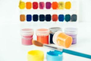 Colorful gouache paints and brush for painting on white background photo