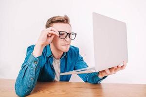 Man in shirt and glasses he looks at laptop in amazement and with a funny face sitting at table on a white background photo