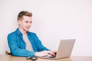 Man in shirt and glasses working on laptop computer sitting at table on a white background photo