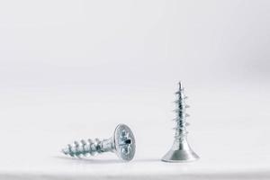 Two metal screws for wood on white wooden background