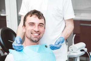 el dentista examina los dientes de un paciente masculino en la silla de un dentista foto