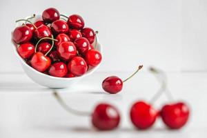 Fresh juicy red cherries in a white plate on the white wooden background. Copy, empty space for text
