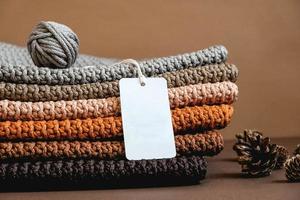 Stack of knitted material from threads of brown, orange, gray colors with an empty price tag on a brown background photo