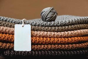 Stack of knitted material from threads of brown, orange, gray colors with an empty price tag on a brown background photo