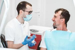el dentista consulta y habla con el paciente masculino en la silla del dentista foto