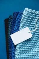 Stack of knitted material from threads of dark blue, light blue, gray colors with blank Price Tag on a blue background photo