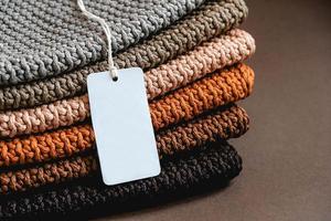 Stack of knitted material from threads of brown, orange, gray colors with an empty price tag on a brown background photo