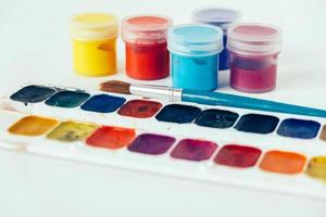 Colorful gouache paints and brush for painting on white background photo