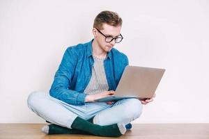 Young man in shirt and glasses working on laptop computer sitting on the table on a white background. Freelance work concept. Copy, empty space for text photo