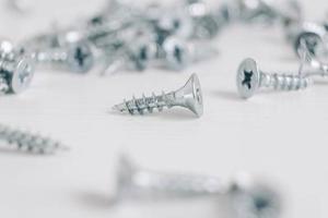 Metal tapping screws for wood on white wooden background. Construction equipment concept photo