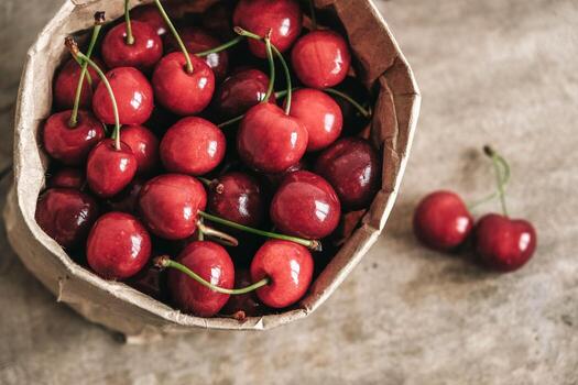 Fresh ripe cherries in a paper bag on wooden background. Top view. Copy, empty space for text photo