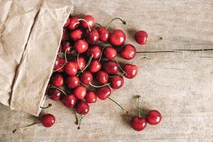 Fresh ripe cherries in a paper bag on wooden background. Top view. Copy, empty space for text photo