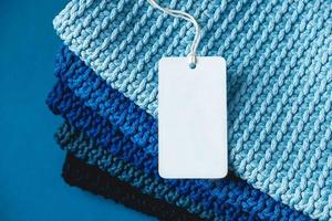 Stack of knitted material from threads of dark blue, light blue, gray colors with blank Price Tag on a blue background photo