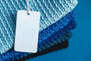 Stack of knitted material from threads of dark blue, light blue, gray colors with blank Price Tag on a blue background photo
