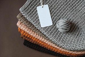 Stack of knitted material from threads of brown, orange, gray colors with an empty price tag on a brown background photo