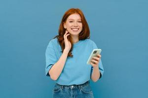 Young ginger-haired woman in blue t-shirt smiling and using her cellphone photo
