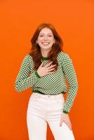Woman with ginger hair in plaid sweater smiling and holding hand on her chest photo