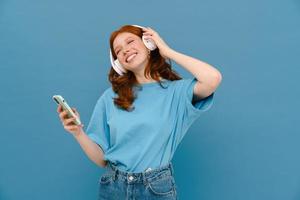 Young ginger-haired woman dancing with cellphone and headphones photo