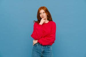 Puzzled ginger-haired woman wearing red sweater looking off to the side photo