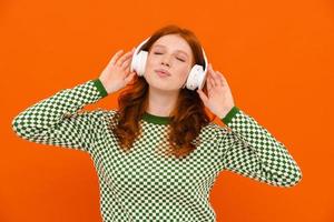 Happy ginger woman in plaid sweater listening music with headphones photo