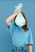 Young woman wearing t-shirt holding plastic trash bag up to her face