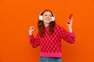 Ginger woman in plaid sweater dancing with cellphone and headphones photo