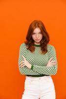 Young ginger-haired woman in plaid sweater posing with her arms crossed photo