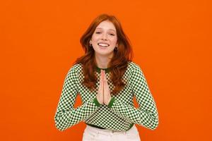 Ginger-haired woman in plaid sweater smiling while making prayer gesture photo