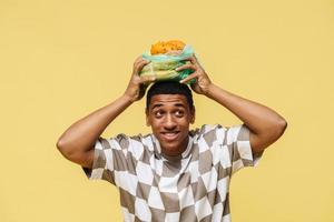 Positive African man holding fruit in plastic trash bag over his head photo