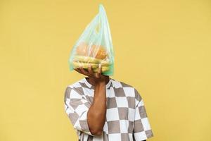 hombre africano sosteniendo una bolsa de basura de plástico con fruta delante de la cara