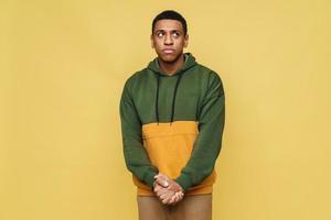 Confused African man in hoodie looking to the side in the yellow studio photo