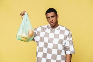 Displeased African man holding plastic trash bag with fruit photo