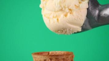 saque el helado de vainilla con una cuchara en el cono de waffle. textura del helado suave en el cono. sobre fondo verde.