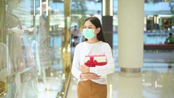 oman wearing protective mask holding a gift box in shopping mall, shopping under Covid-19 pandemic, thanksgiving and Christmas concept. video