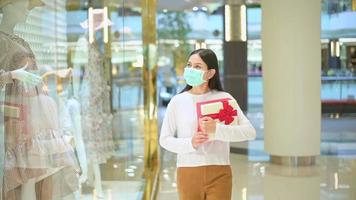 mulher usando máscara protetora segurando uma caixa de presente no shopping, fazendo compras sob o conceito de pandemia covid-19, ação de graças e natal.