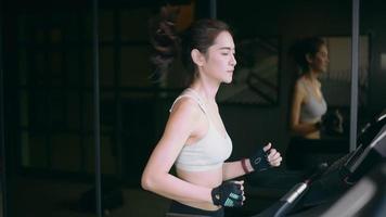jonge Aziatische vrouw draait op een loopband op sportschool. slow motion video