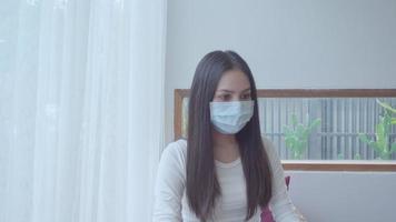 een jonge vrouw draagt een gezichtsmasker en werkt met een laptop thuis, werk vanuit huis concept video