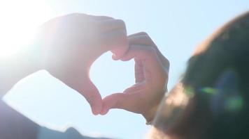 hand av glad liten flicka vid solnedgången. glad liten flickas hand sträckte ut och gjorde en hjärtform till solens siluett solljus. hjärta symbol för familjens kärlek. video