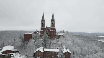 Aerial view of church with steeple and spires in winter forest full of trees covered in snow video