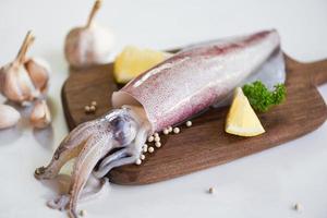 Raw squid on cutting board with salad spices lemon garlic on the white plate background - fresh squids octopus or cuttlefish for cooked food at restaurant or seafood market photo