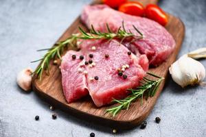 Raw pork meat on wooden cutting board at kitchen table for cooking pork steak roasted or grilled with ingredients herb and spices - Fresh pork photo