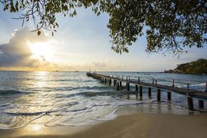 increíble playa tropical de arena con un puente de madera de silueta fuera de la playa tropical - paseo marítimo o pasarela de madera hasta el horizonte en el paisaje del paraíso marino, amanecer o atardecer mar cielo dramático foto