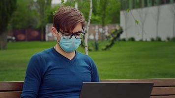 man arbetar på sin bärbara dator under pandemin, medan han satt på en bänk utomhus. video