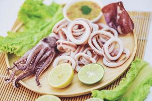 squid rings on wooden plate, Fresh squid cooked boiled with lettuce vegetable salad lemon and seafood sauce on table background photo