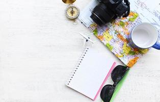 concepto de fondo de viaje planificación artículos de viaje de vacaciones esenciales accesorios de viaje de verano con cámara gafas de sol brújula mapa cuaderno taza de café y avión para viajeros en madera blanca foto