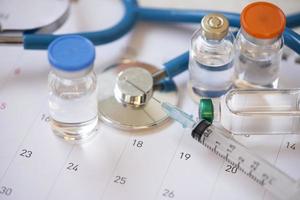 Medical tools with vaccine syringe injection medication drug and stethoscope on calendar - Medicine and health concept